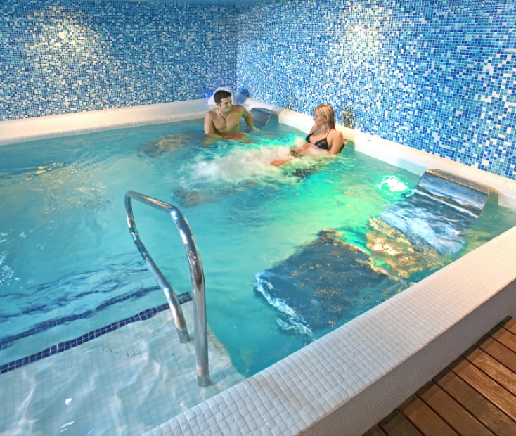 hotel spa villa pasiega Pareja tumbada en hamacas sumergidas en la piscina con hidromasaje